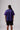 A back shot of a male model wearing the PONY Purple Striped Away jersey, black shorts, and PONY M100 sneakers standing in a studio.